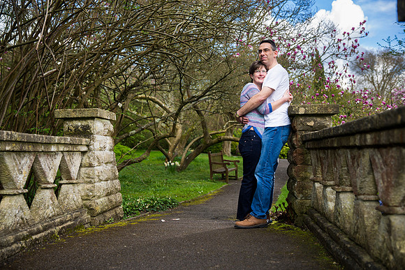 Portrait-couple-cuddling-park-bridge-trees-blue-sky