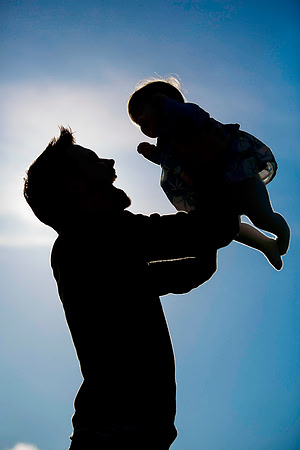 Silhoette of dad holding baby daughter in air with blue sky