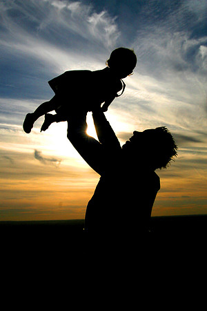 Silhoette of dad holding daughter in air at sunset